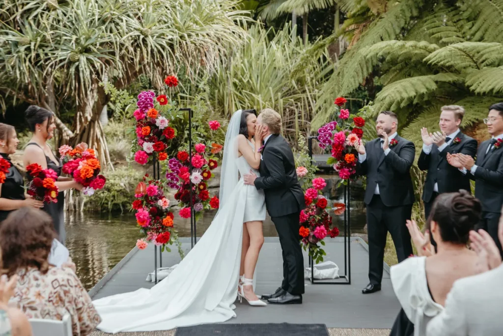 bride and groom first kiss after ceremony at Australian Botanic Garden Mount Annan with red floral arch
