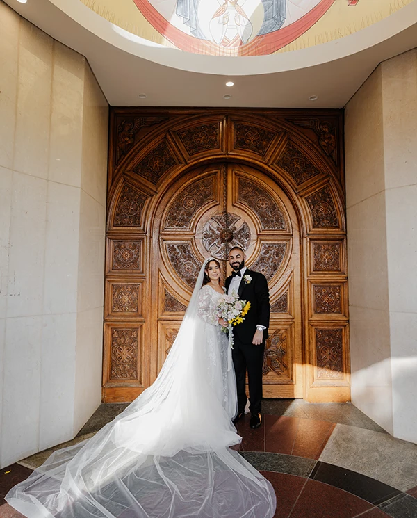 Bride standing in front of ornate wooden doors outside the church