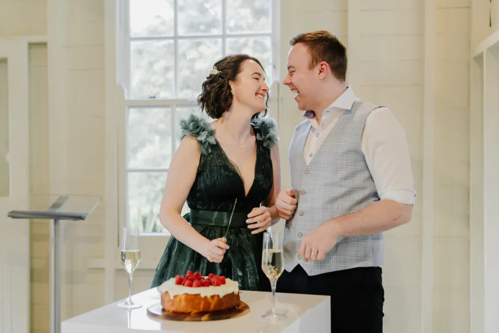 Couple cutting the wedding cake inside Athol Hall with sash windows in the background